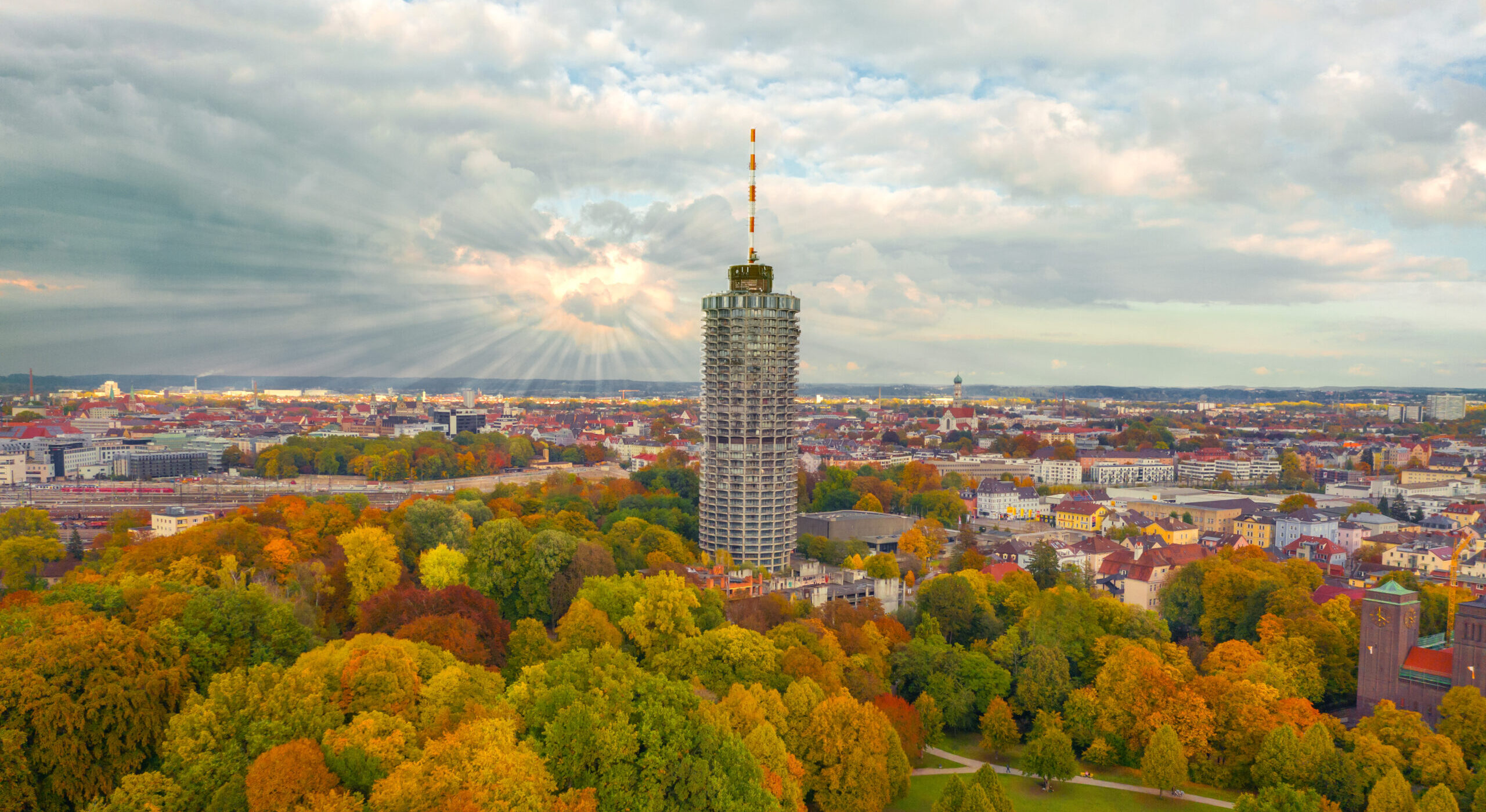 Blick auf Augsburg und den Hotelturm mit herbstlichen Bäumen und Sonnenstrahlen